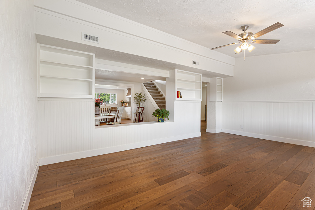 Empty room with wood-type flooring, baseboards, stairway, ceiling fan, and a wainscoted wall