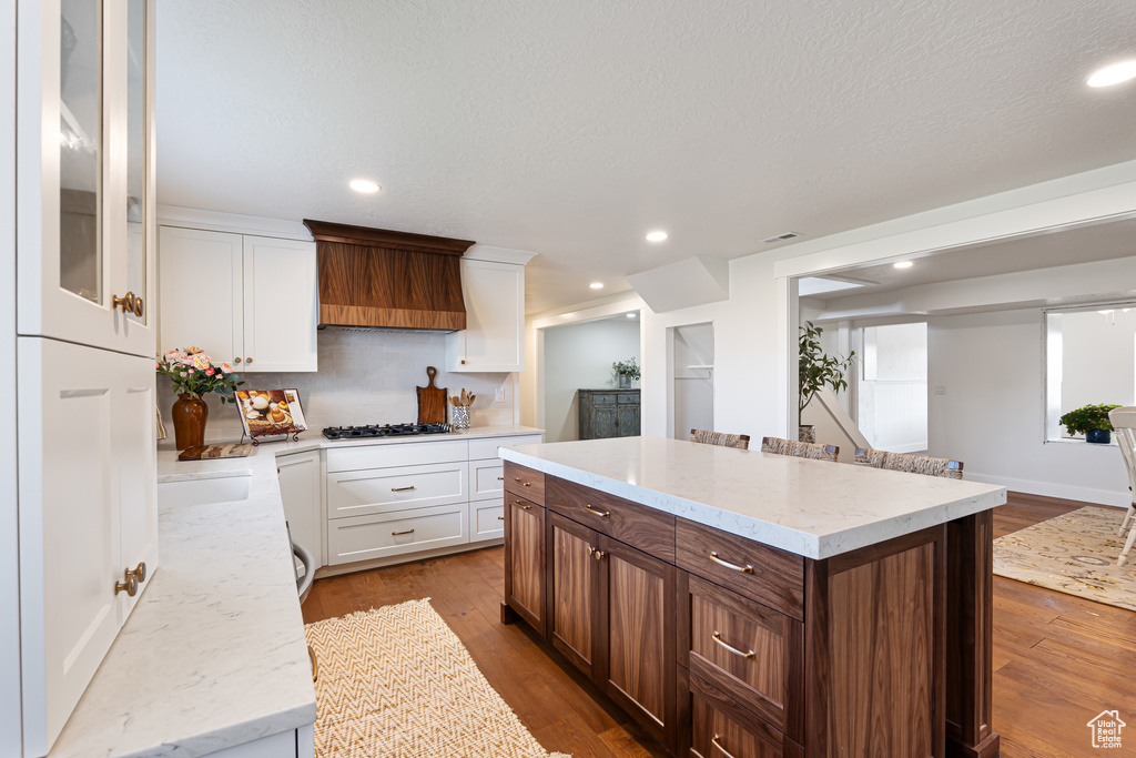 Kitchen with white cabinetry, wood finished floors, a kitchen island, recessed lighting, and light stone countertops