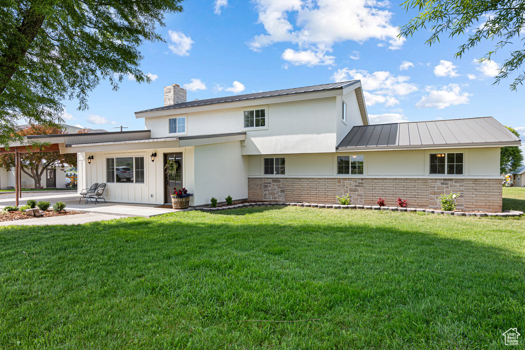 View of front of house with a chimney, a patio, a front yard, a standing seam roof, and stucco siding