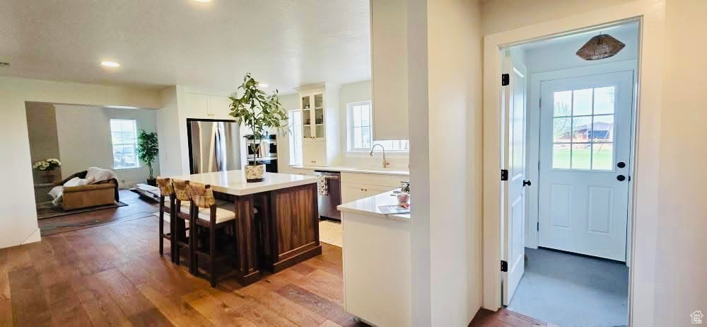 Kitchen with appliances with stainless steel finishes, a sink, light countertops, a center island, and glass insert cabinets