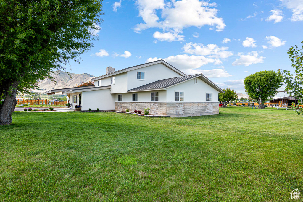 Rear view of property featuring stucco siding, a lawn, a chimney, and a patio area