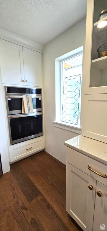 Kitchen featuring a textured ceiling, light stone countertops, double oven, dark wood-style floors, and white cabinetry