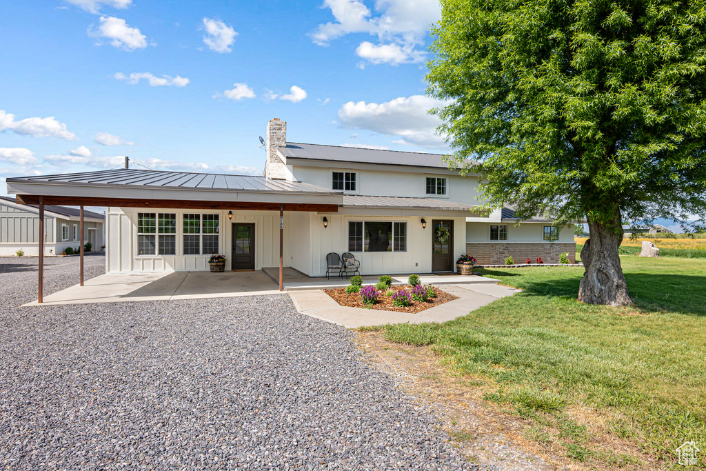 Back of property featuring a chimney, a lawn, metal roof, a standing seam roof, and a patio area