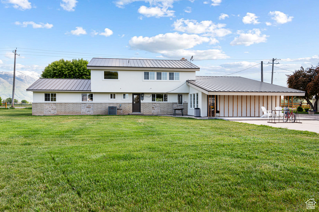 Rear view of property with a yard, a patio, central air condition unit, and metal roof