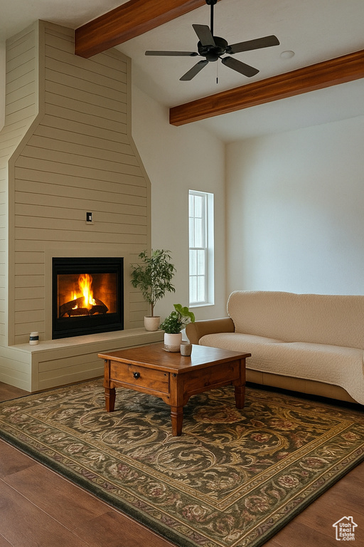 Living area with a large fireplace, ceiling fan, beamed ceiling, and wood finished floors