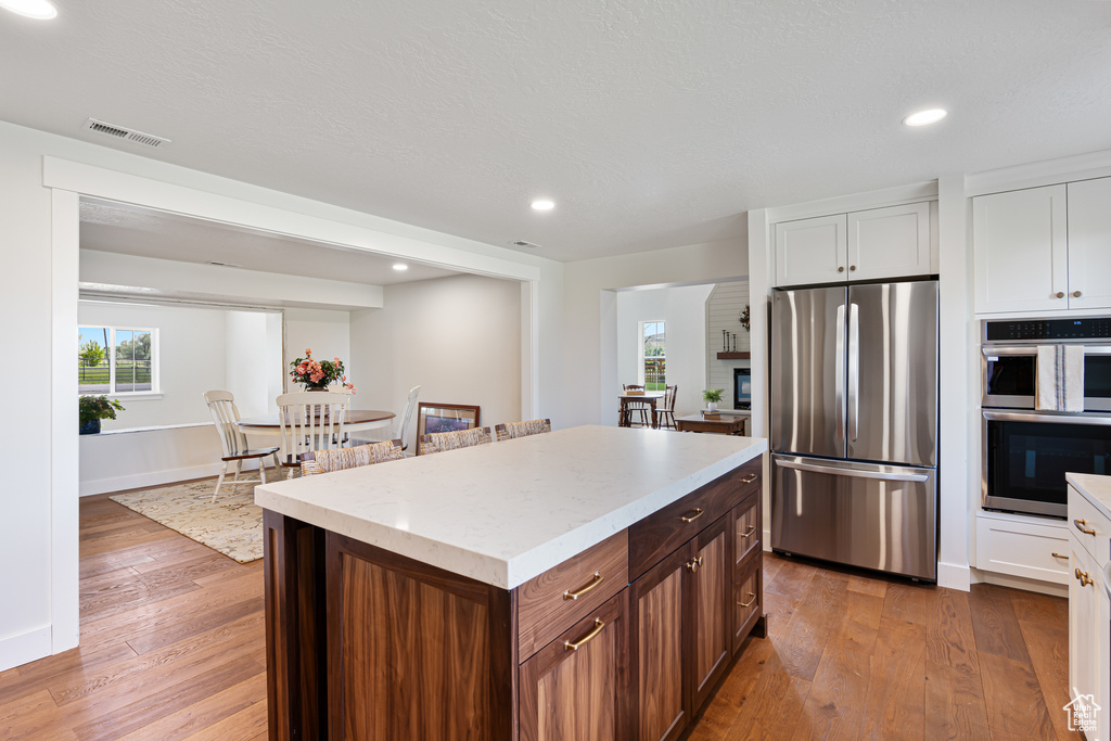 Kitchen featuring appliances with stainless steel finishes, hardwood / wood-style floors, white cabinetry, a center island, and recessed lighting