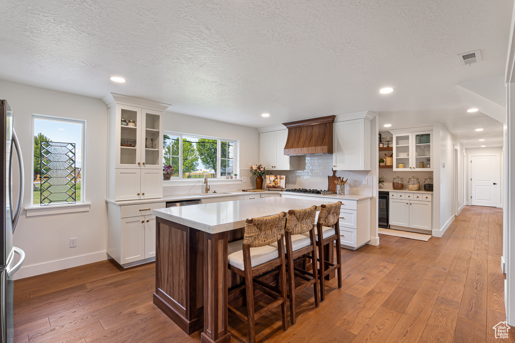 Kitchen featuring a sink, hardwood / wood-style flooring, a textured ceiling, white cabinetry, and premium range hood