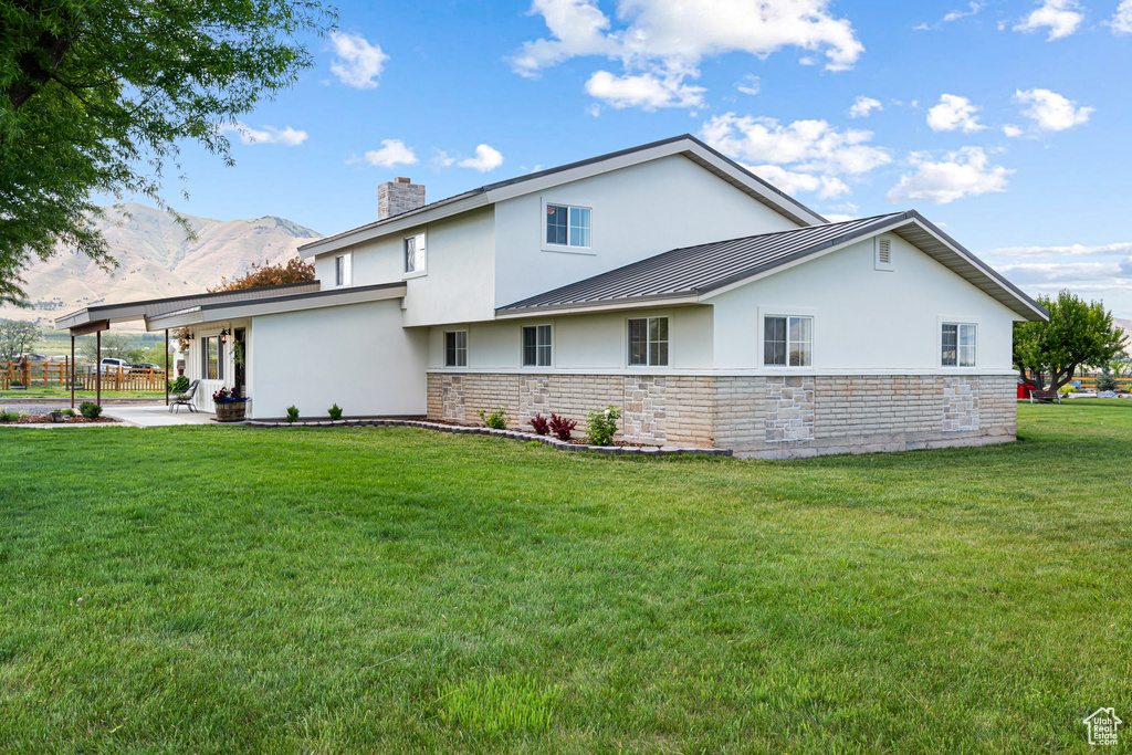 View of side of property featuring stucco siding, a chimney, a patio area, a lawn, and a standing seam roof