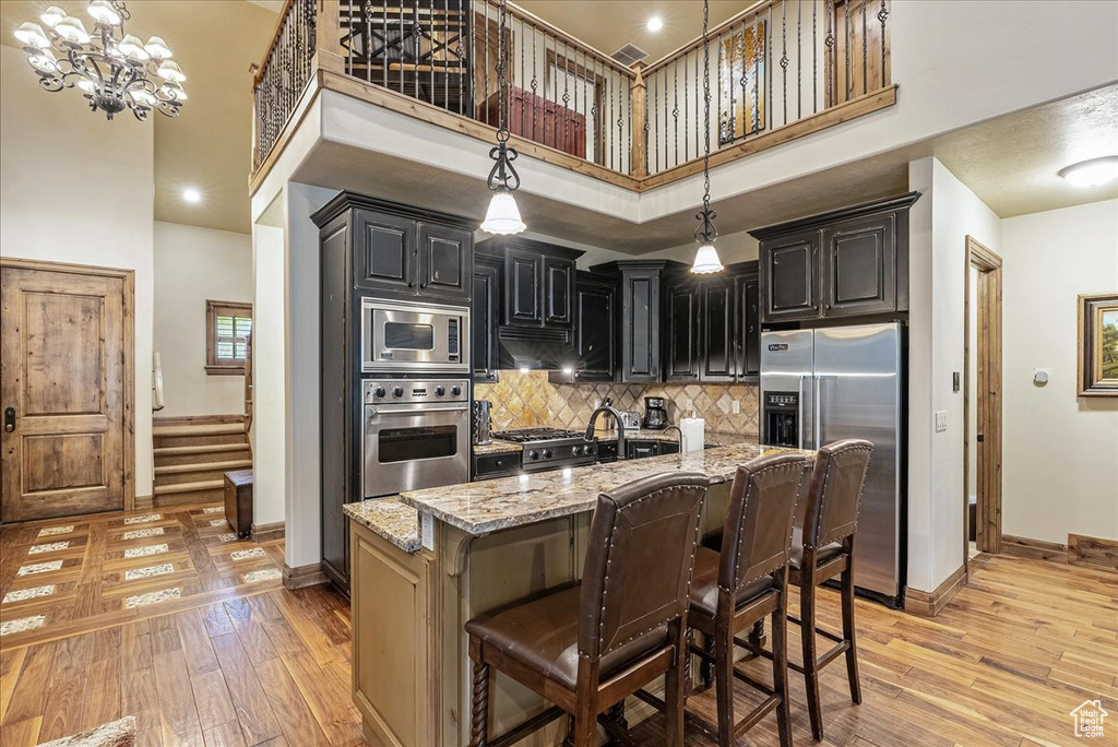 Kitchen featuring appliances with stainless steel finishes, baseboards, light stone counters, light wood-style flooring, and a high ceiling
