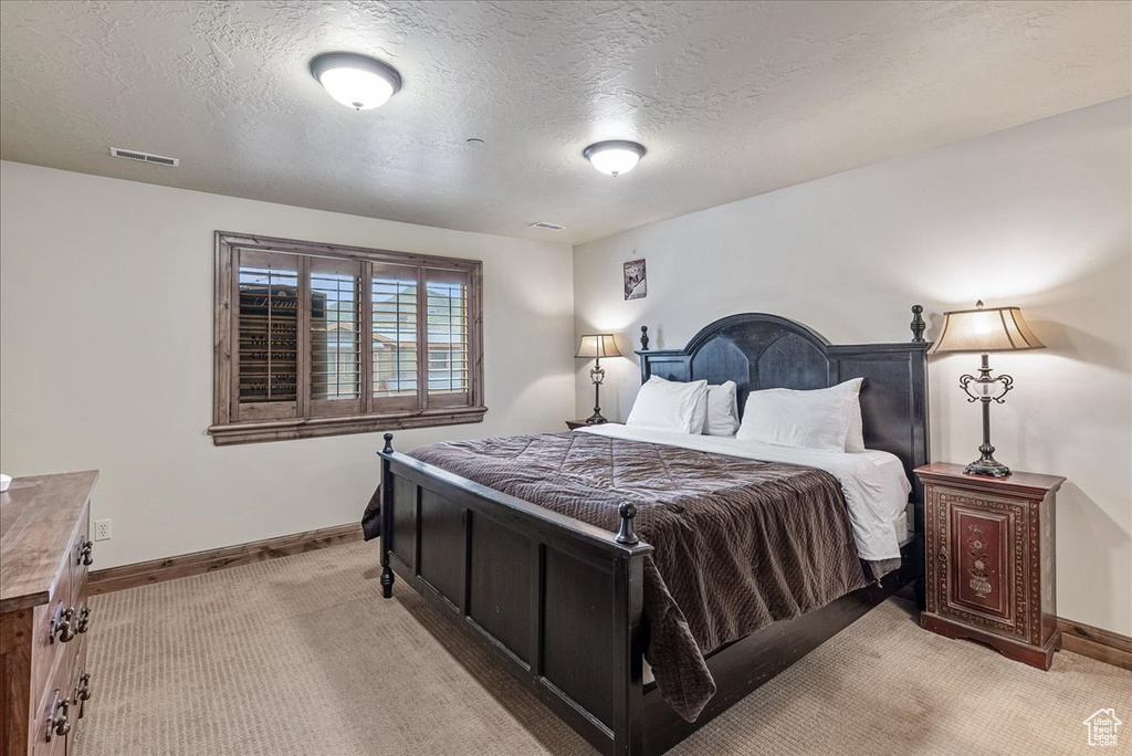 Bedroom featuring light carpet, baseboards, and a textured ceiling