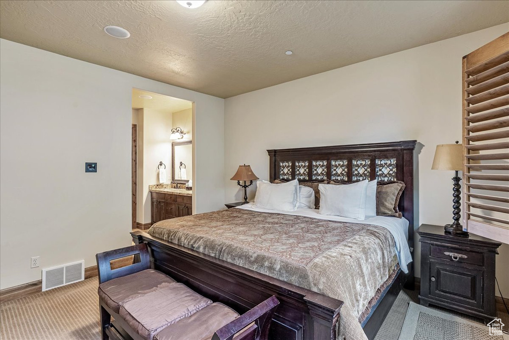 Carpeted bedroom with baseboards, ensuite bathroom, and a textured ceiling