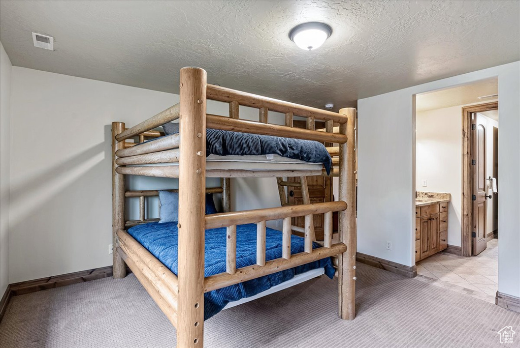 Bedroom featuring light colored carpet, baseboards, a textured ceiling, and ensuite bathroom