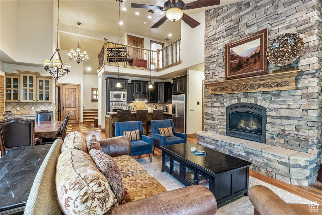 Living area with a high ceiling, a chandelier, ceiling fan, a stone fireplace, and recessed lighting