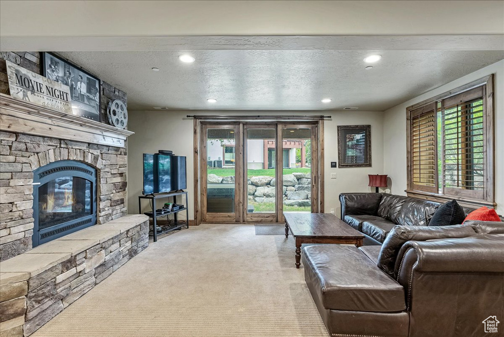 Living area with carpet, a stone fireplace, plenty of natural light, a textured ceiling, and recessed lighting