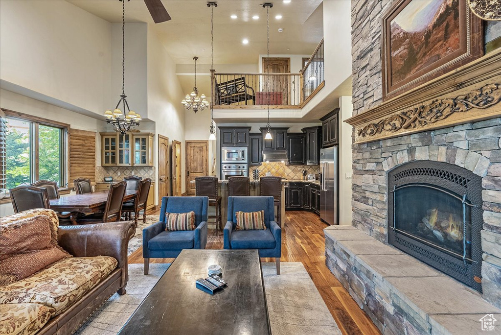 Living area with a towering ceiling, light wood-style flooring, a fireplace, a chandelier, and a ceiling fan