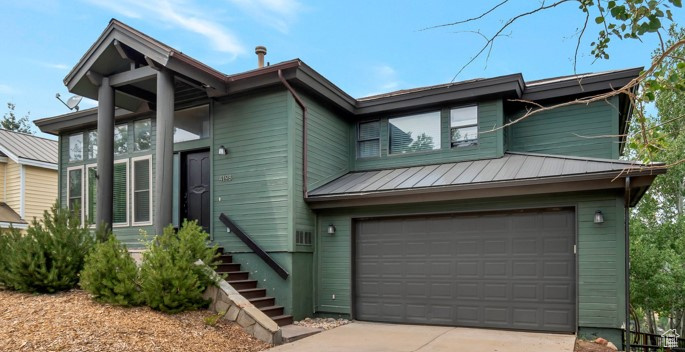 View of front of property with an attached garage, a standing seam roof, driveway, and metal roof