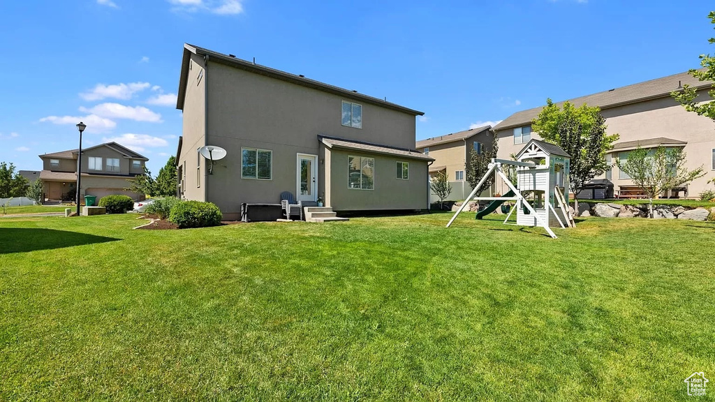 Rear view of property featuring a yard, a playground, and stucco siding