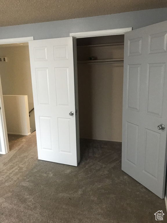 Unfurnished bedroom featuring a textured ceiling, dark carpet, and a closet