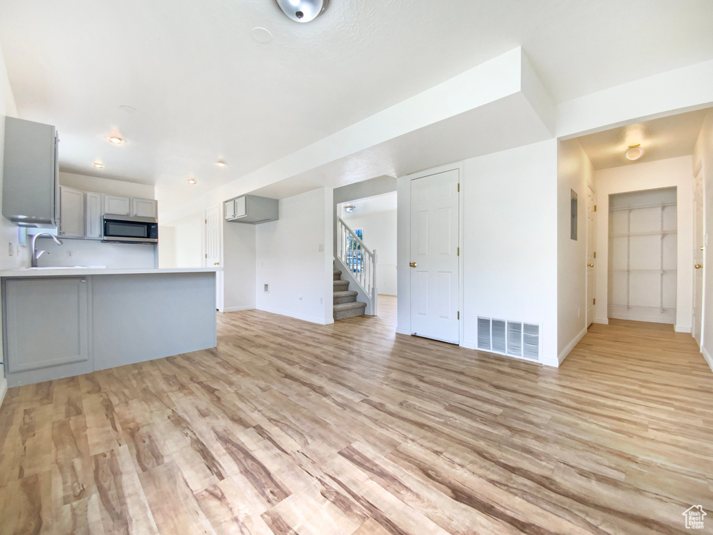 Unfurnished living room featuring a sink, baseboards, visible vents, light wood-style floors, and stairs