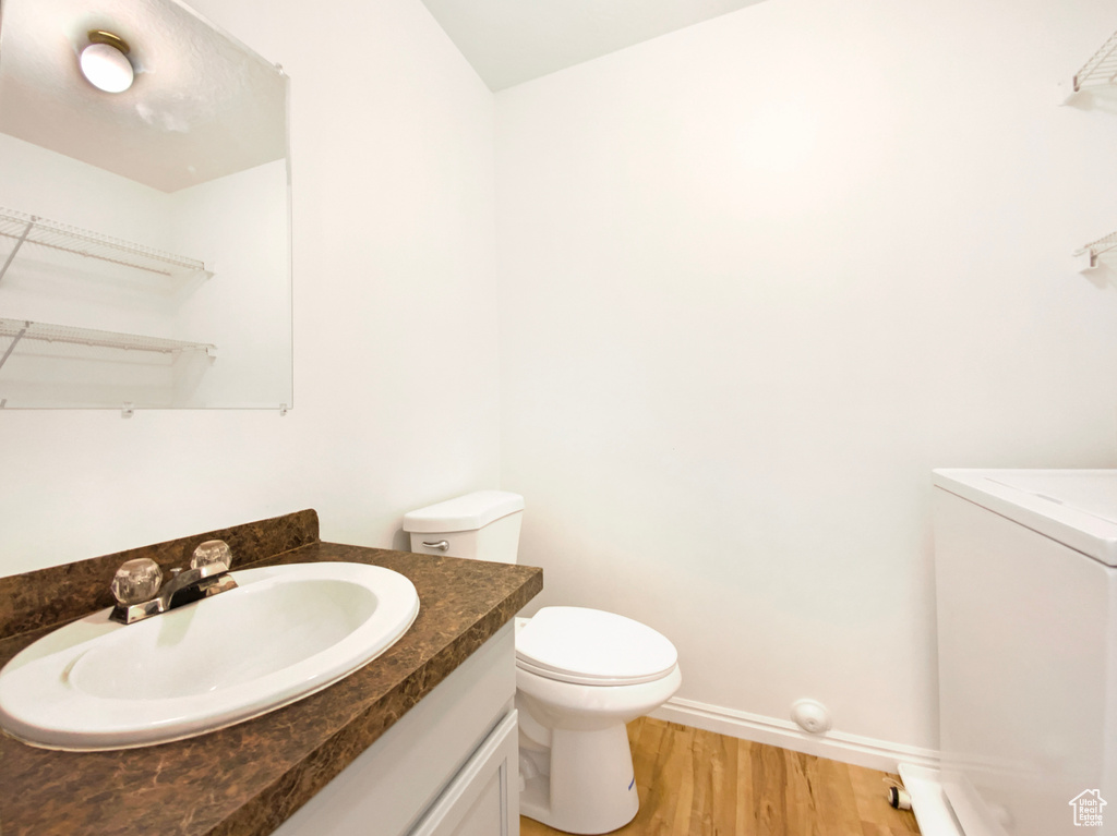 Bathroom featuring wood finished floors, vanity, baseboards, toilet, and washer / clothes dryer