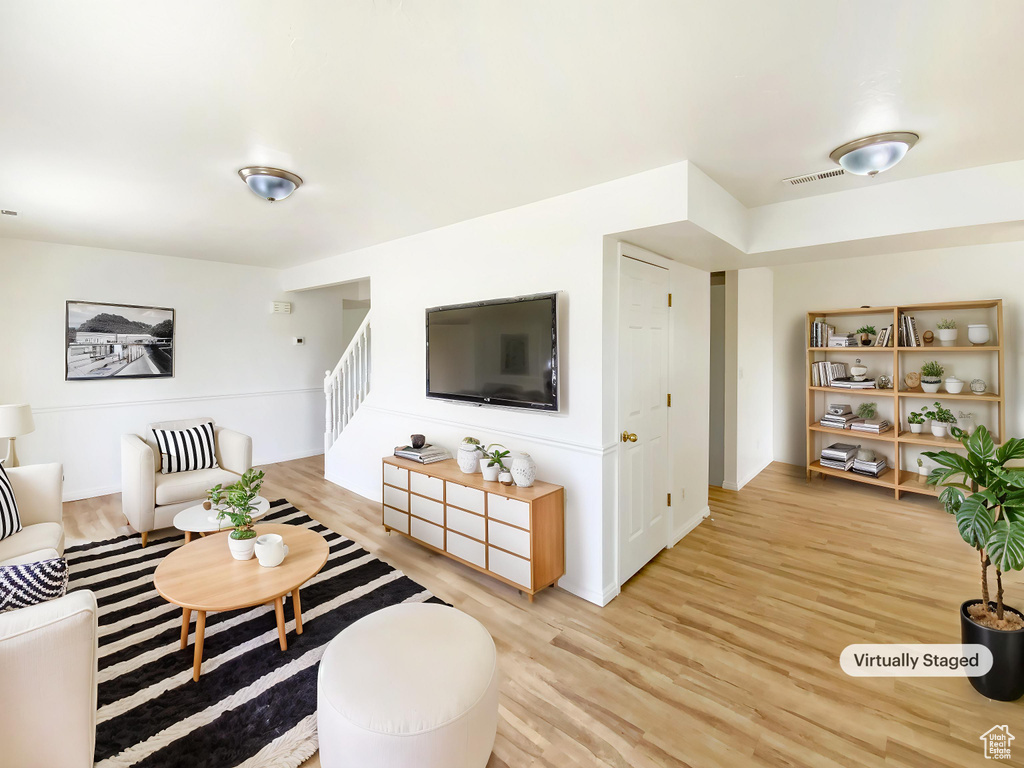 Living room featuring baseboards, visible vents, light wood finished floors, and stairs