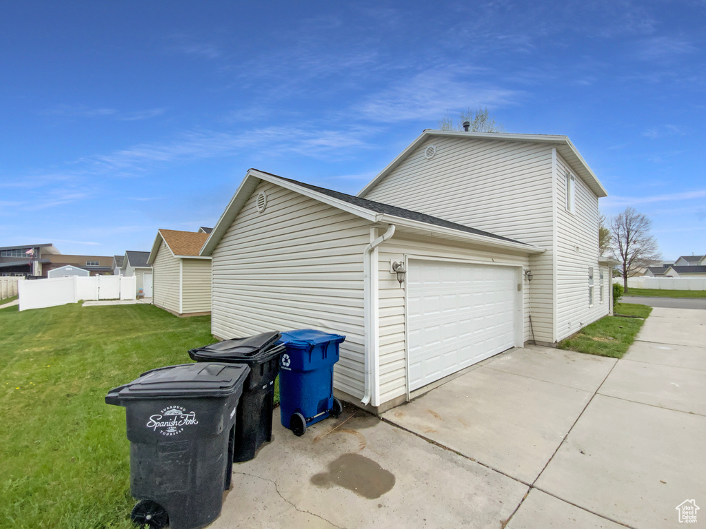 View of side of home with an attached garage, driveway, fence, and a lawn