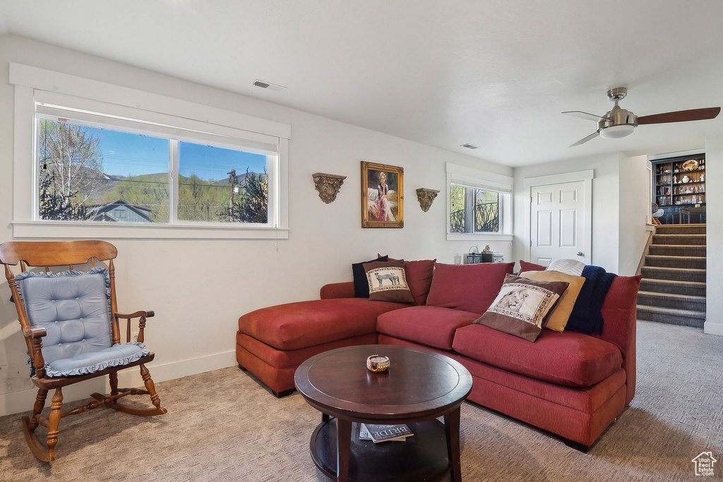 Carpeted living area with stairway, baseboards, visible vents, and ceiling fan