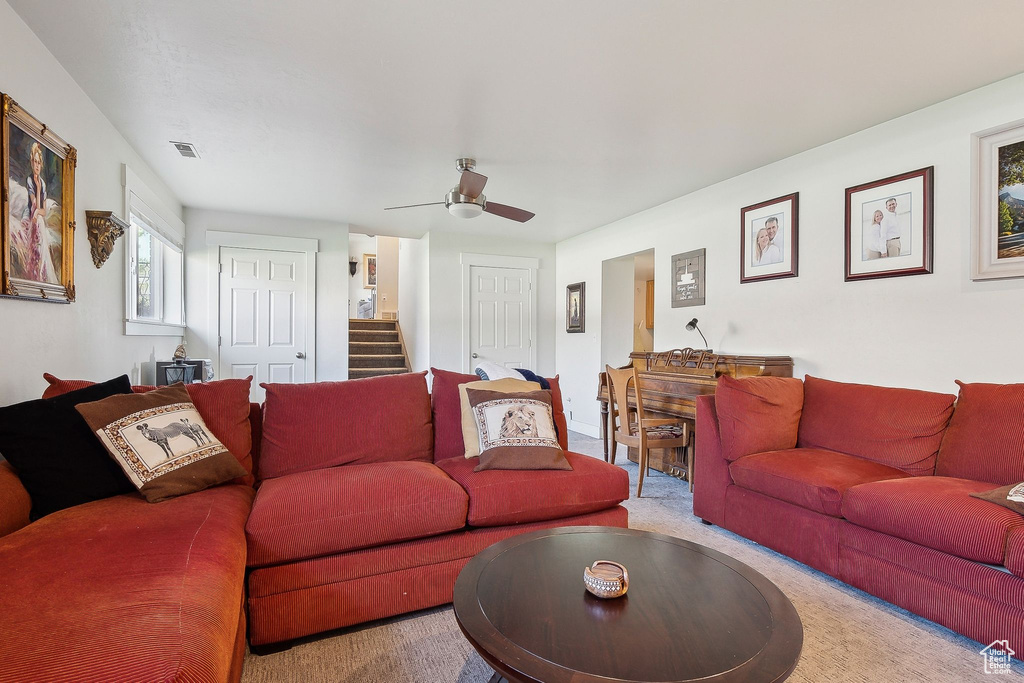 Living room featuring carpet, visible vents, stairs, and ceiling fan
