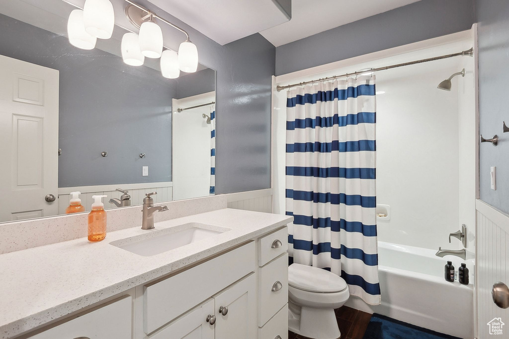 Bathroom with wood finished floors, wainscoting, vanity, toilet, and shower / bath combo with shower curtain