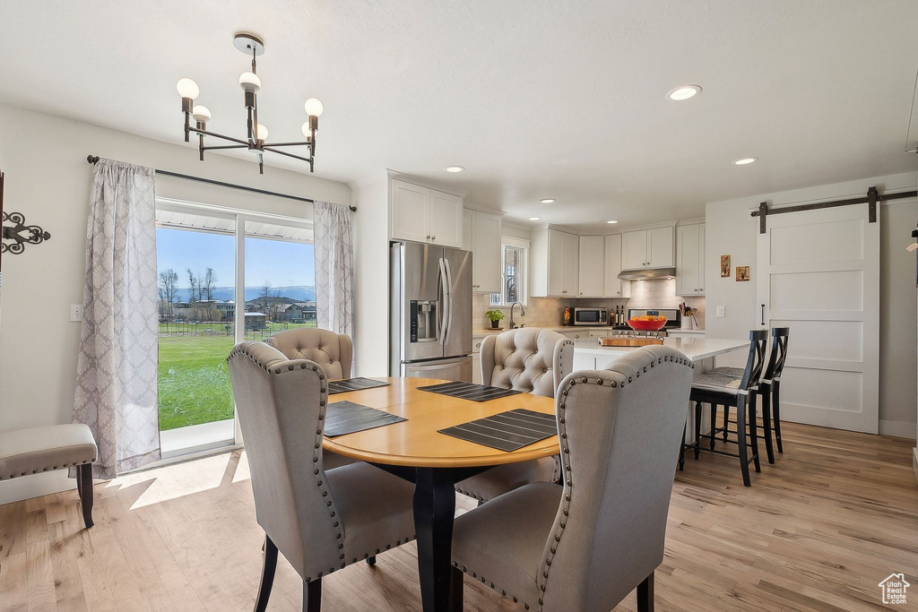 Dining room featuring a barn door, a notable chandelier, light wood finished floors, and recessed lighting