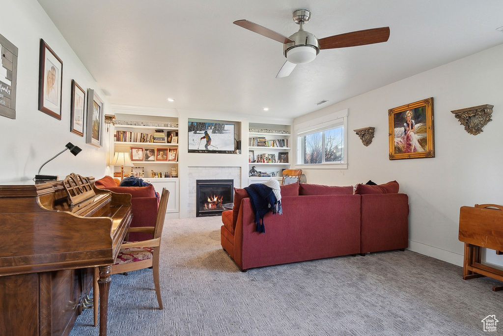 Carpeted living room with built in shelves, ceiling fan, a glass covered fireplace, and visible vents