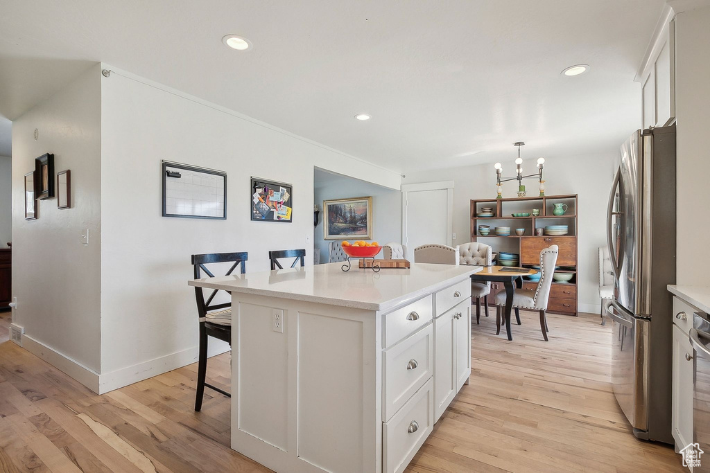 Kitchen with light wood finished floors, an inviting chandelier, freestanding refrigerator, a breakfast bar area, and white cabinetry