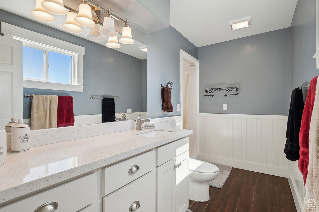 Bathroom with a wainscoted wall, wood finished floors, vanity, and toilet