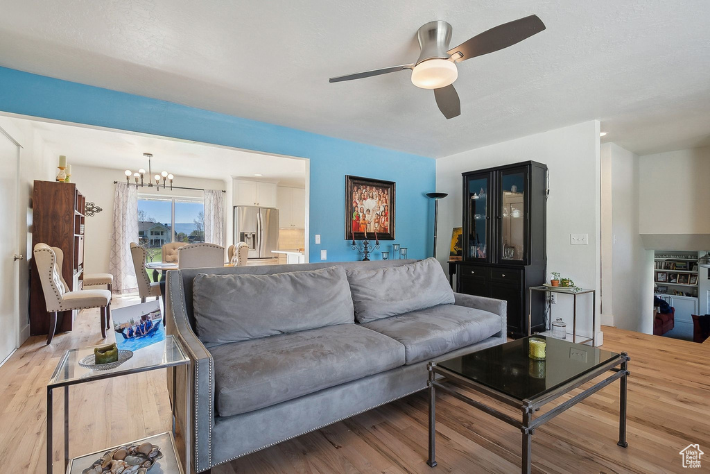 Living room with ceiling fan with notable chandelier and light wood-type flooring
