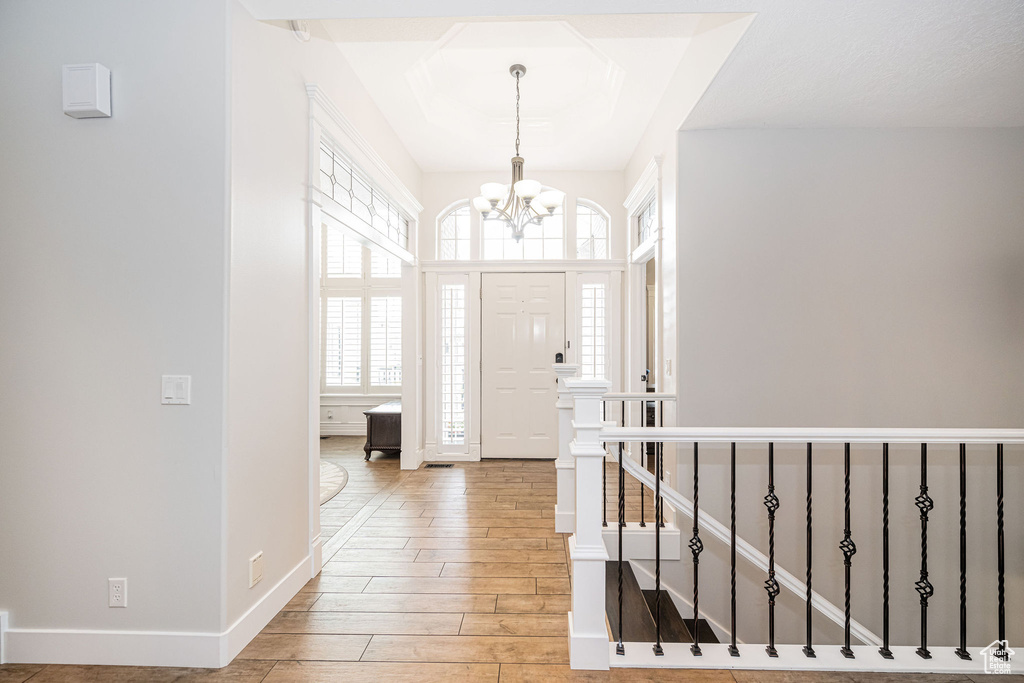 Entrance foyer featuring light wood-type flooring, baseboards, a notable chandelier, and a tray ceiling