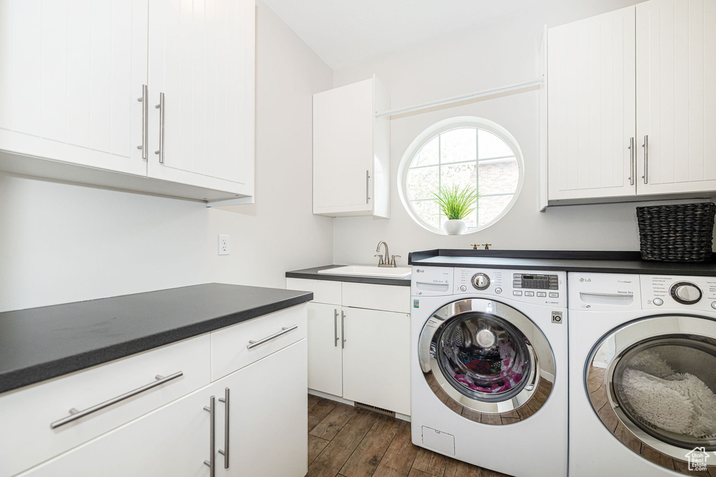 Washroom featuring a sink, washer and clothes dryer, dark wood-type flooring, and cabinet space