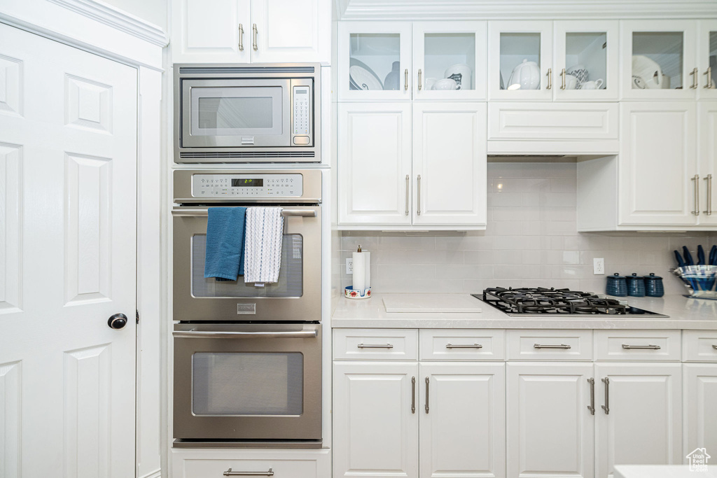 Kitchen featuring white cabinets, appliances with stainless steel finishes, tasteful backsplash, and light countertops
