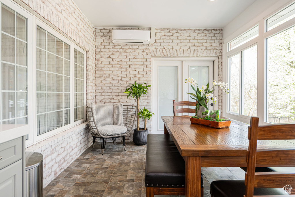 Sunroom / solarium with a wall mounted air conditioner, stone finish flooring, and brick wall