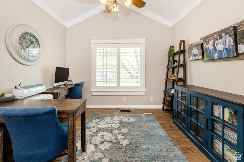 Home office with vaulted ceiling, visible vents, wood finished floors, baseboards, and ceiling fan