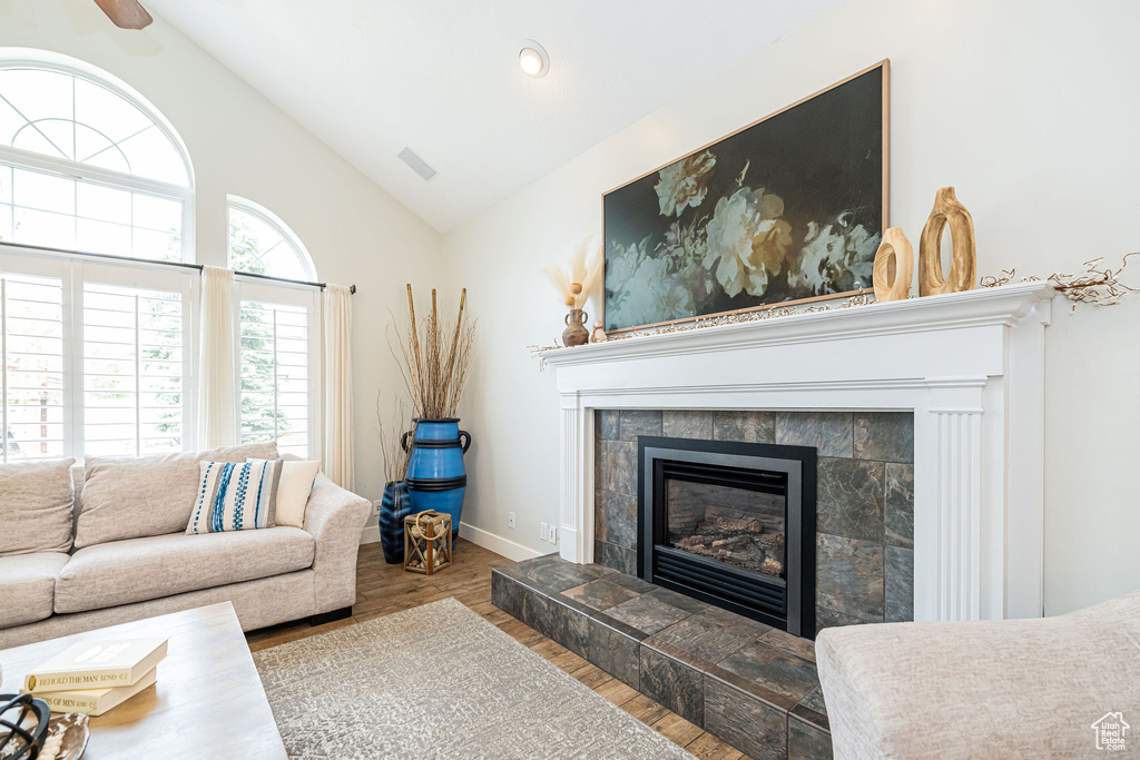Living room featuring vaulted ceiling, visible vents, baseboards, wood finished floors, and a tile fireplace