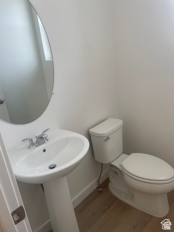 Half bathroom featuring wood finished floors, toilet, and baseboards