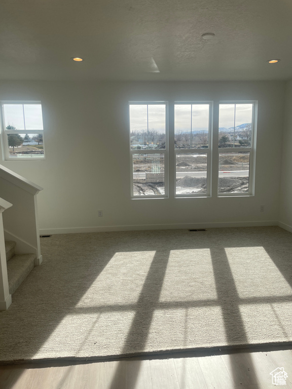 Carpeted empty room with visible vents, baseboards, stairway, and a healthy amount of sunlight
