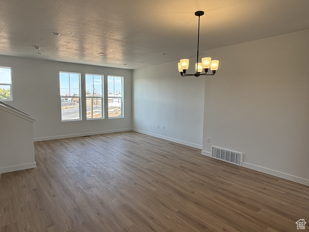 Empty room featuring an inviting chandelier, wood finished floors, visible vents, and baseboards