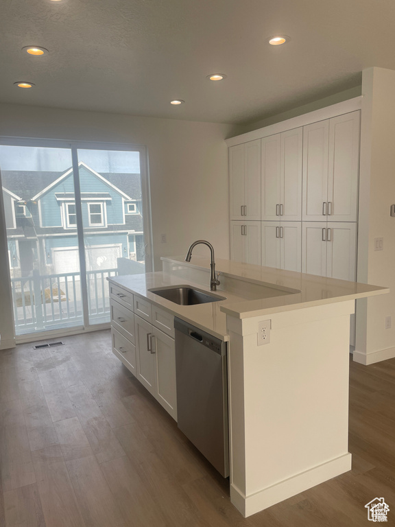 Kitchen with stainless steel dishwasher, white cabinetry, wood finished floors, and a sink