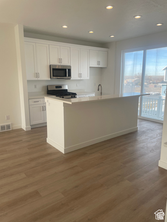 Kitchen with white cabinets, light wood finished floors, stainless steel appliances, and visible vents