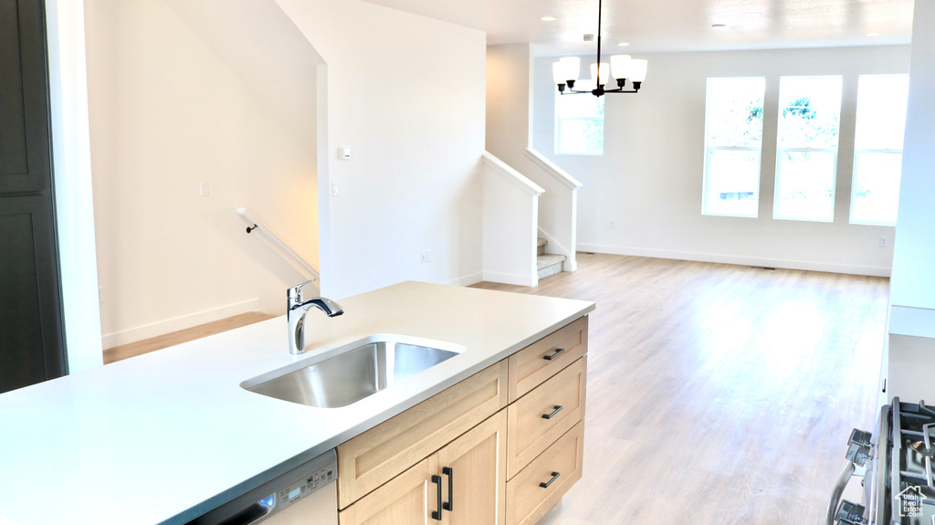 Kitchen featuring an inviting chandelier, light countertops, a sink, light wood-type flooring, and pendant lighting