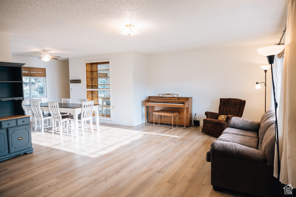 Living room featuring light wood-type flooring, a textured ceiling, a ceiling fan, and baseboards