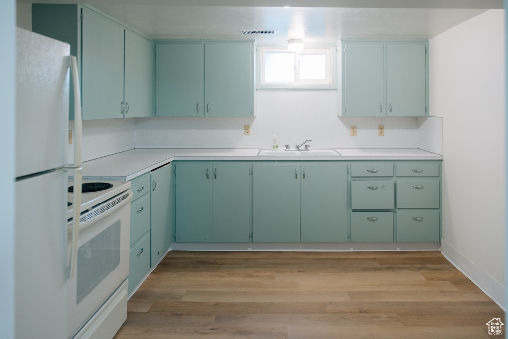 Kitchen featuring light wood-style flooring, a sink, white appliances, and light countertops