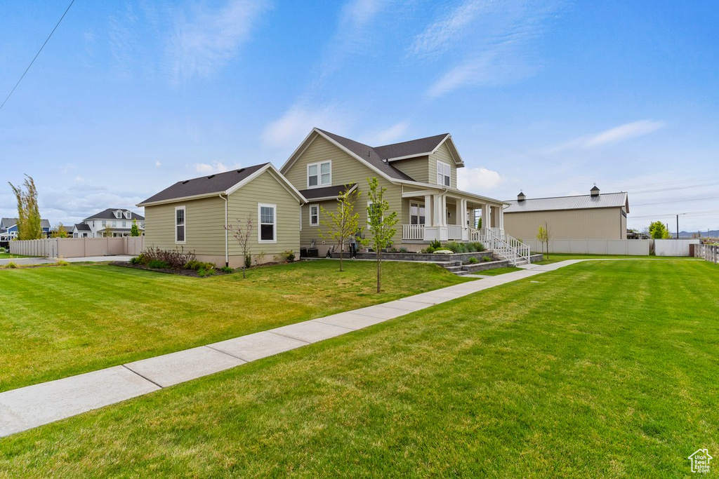 View of front of home with covered porch, fence, and a front lawn
