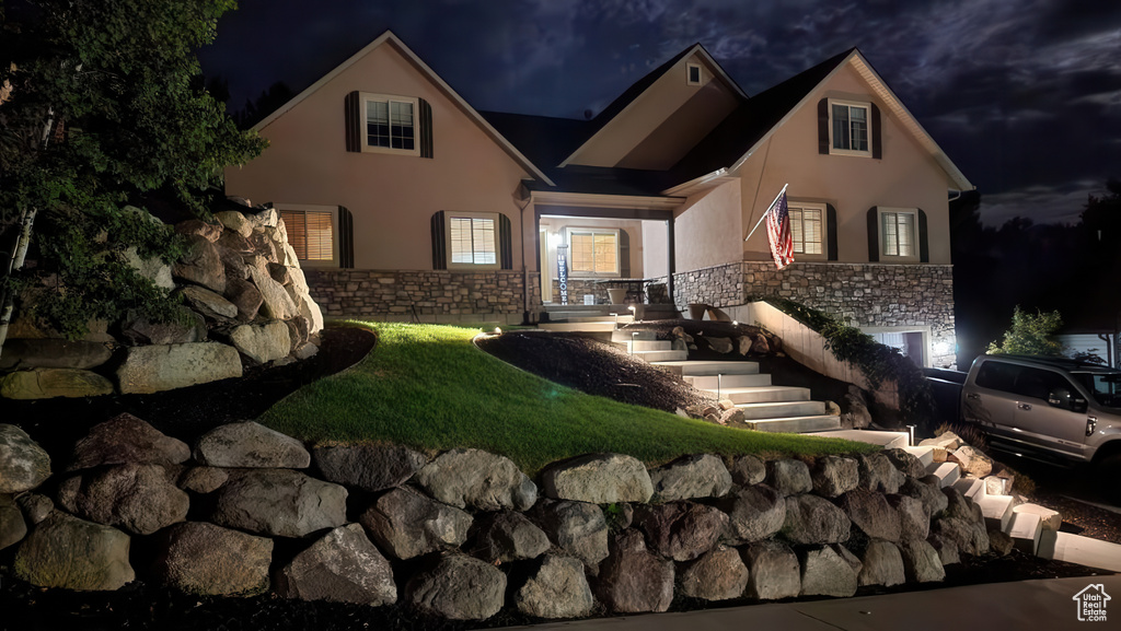 Back of house at twilight featuring stucco siding and stone siding